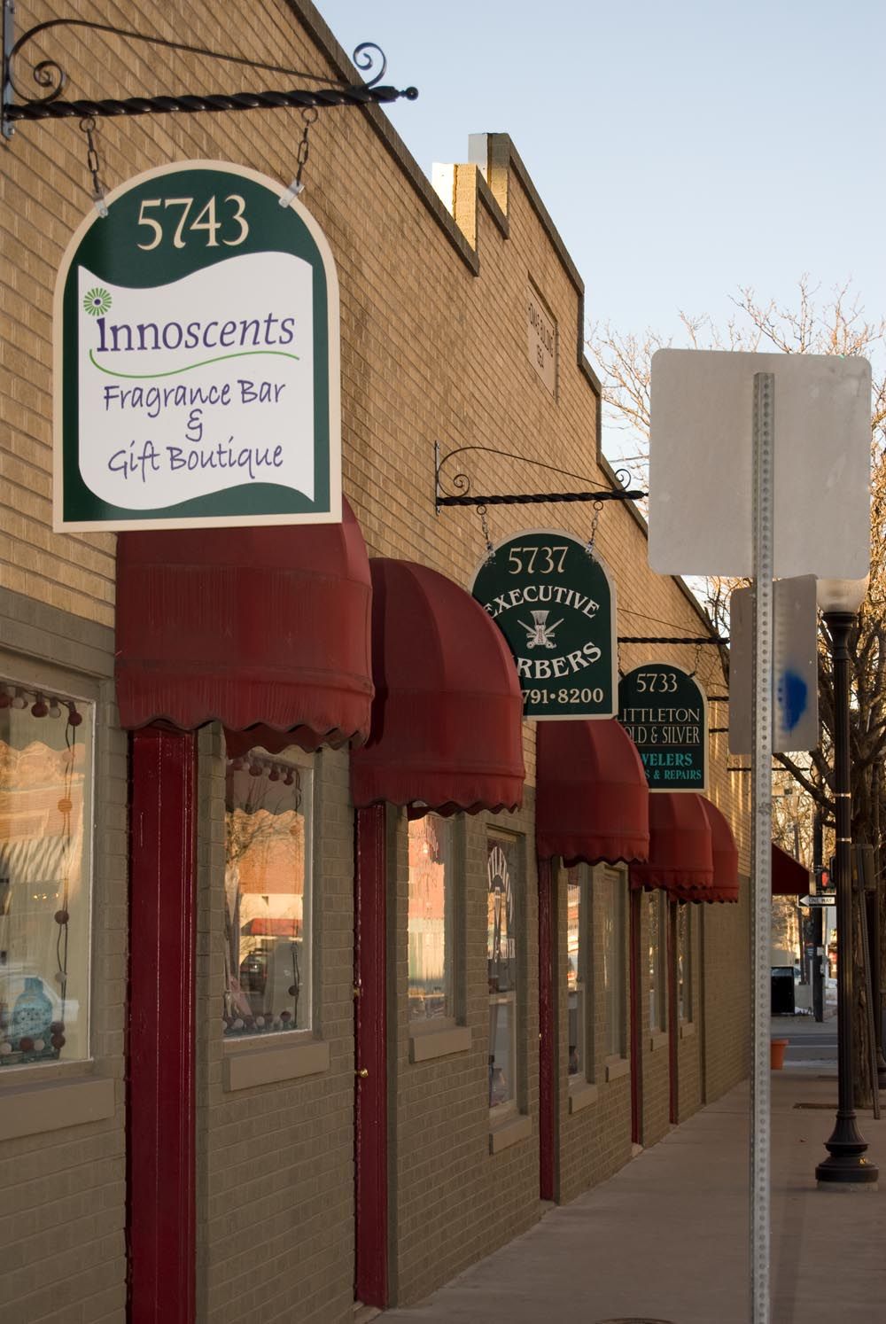 Row of boutique storefronts with burgundy awnings and shop signs along a retail street.