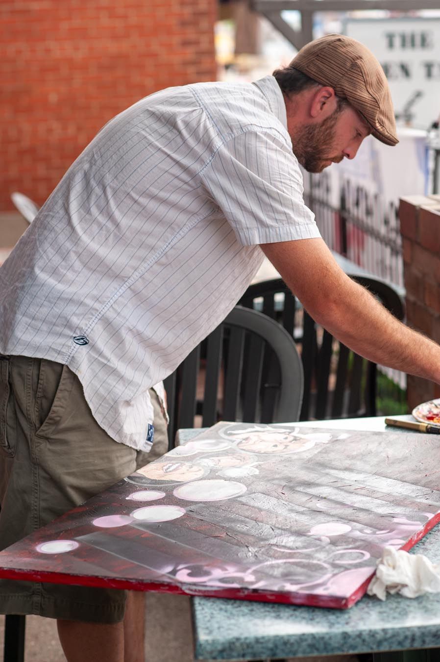 Person leaning over table working on art project against brick wall.