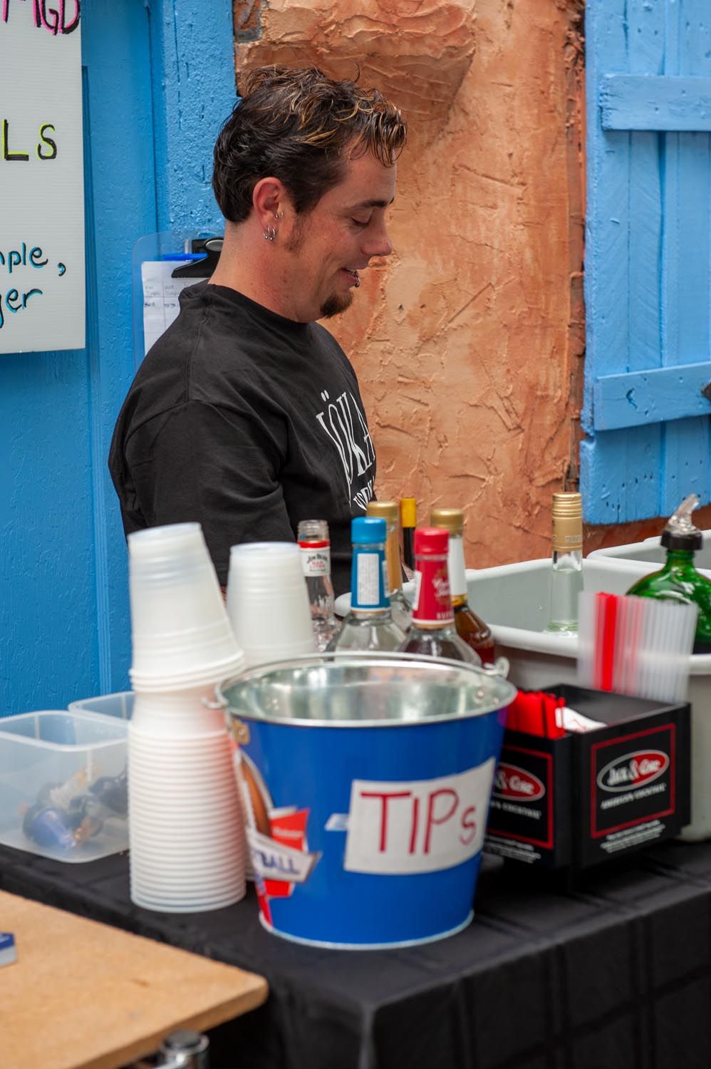 A beverage service station with blue walls, disposable cups, and various drink containers arranged on a black table.