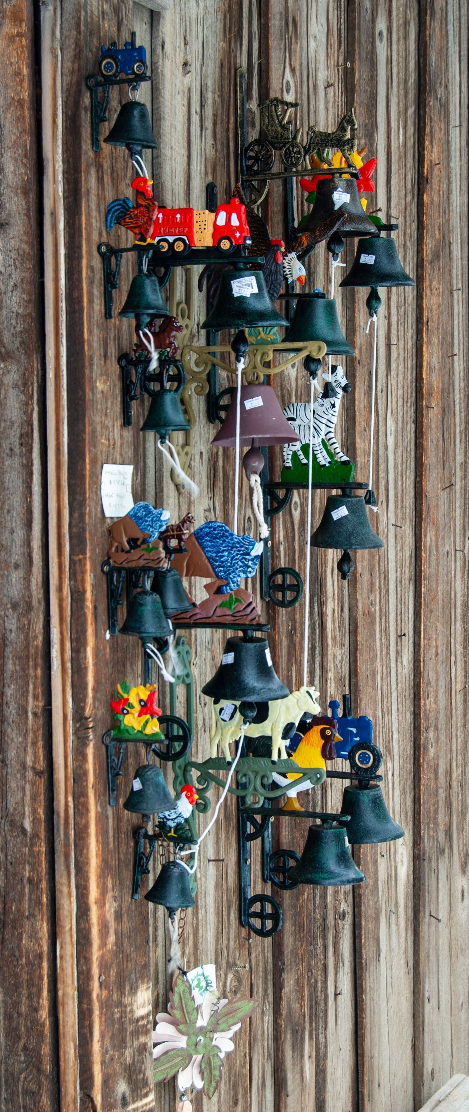 Decorative vintage bells and ornaments hanging on a rustic wooden wall display.