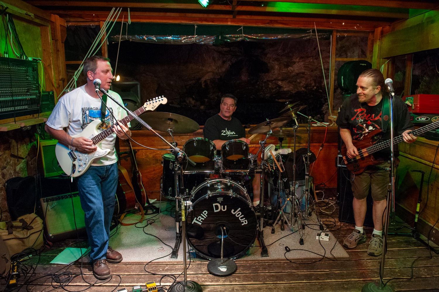 Three musicians performing with guitars and drums in a dimly lit basement venue.