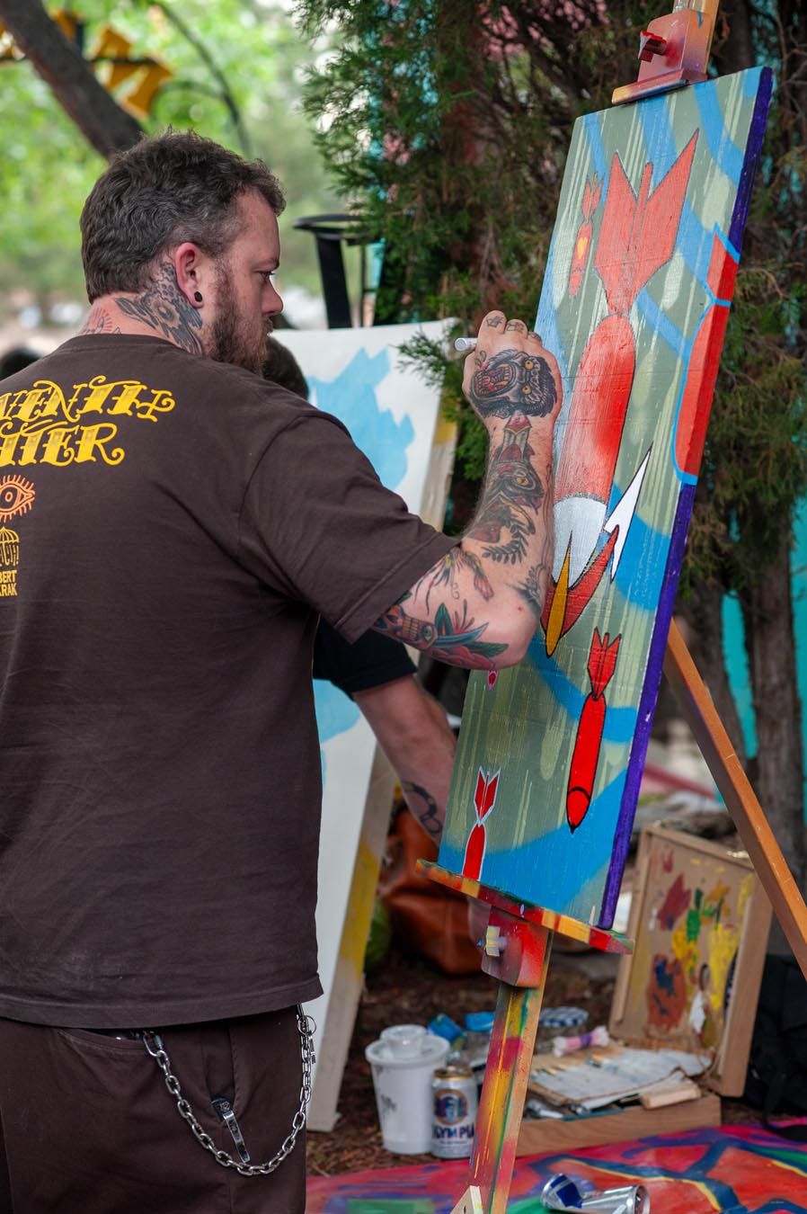 Artist working on colorful painting at outdoor easel.