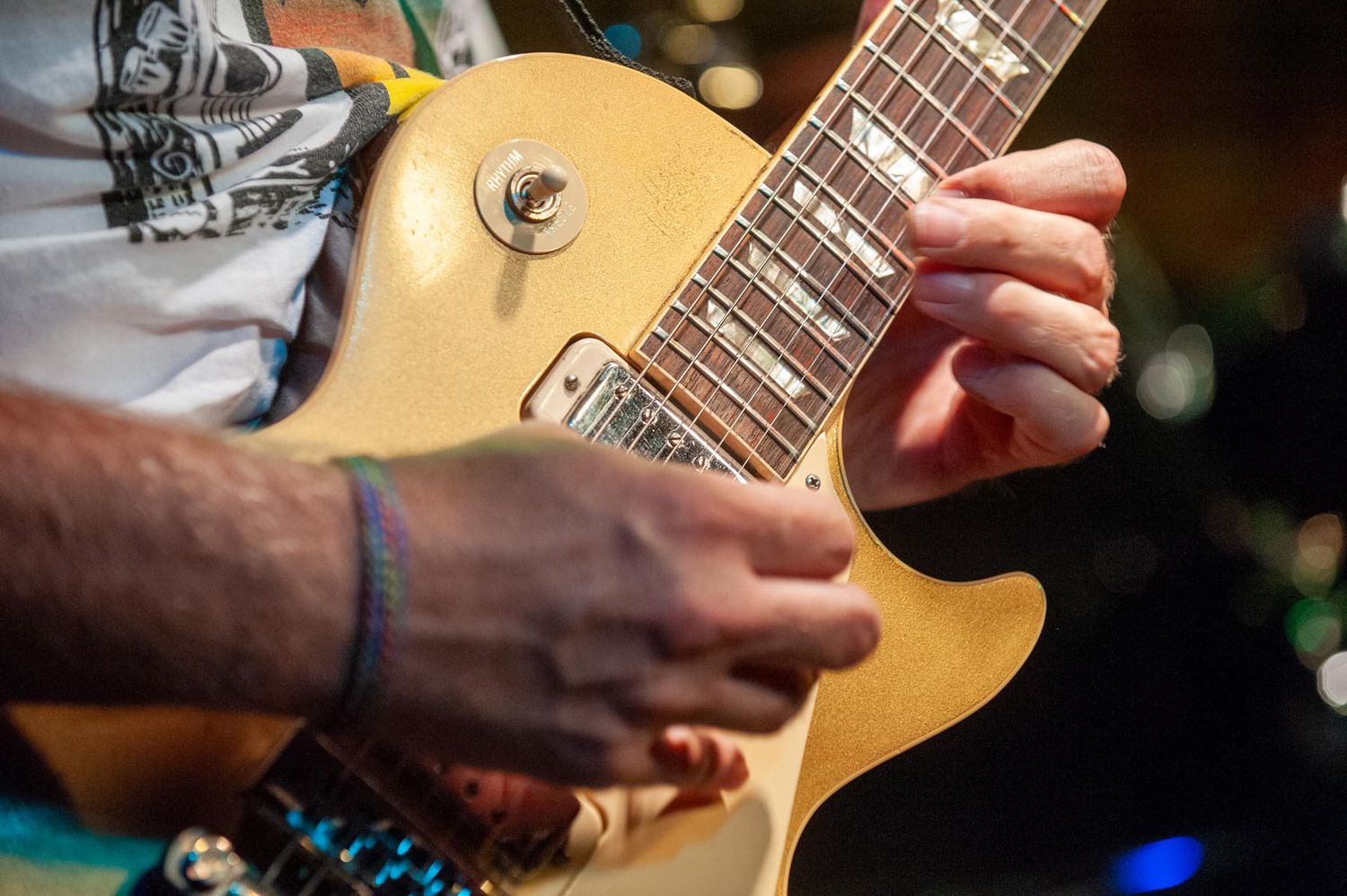 Close-up shot of hands playing a gold Les Paul electric guitar during a performance.