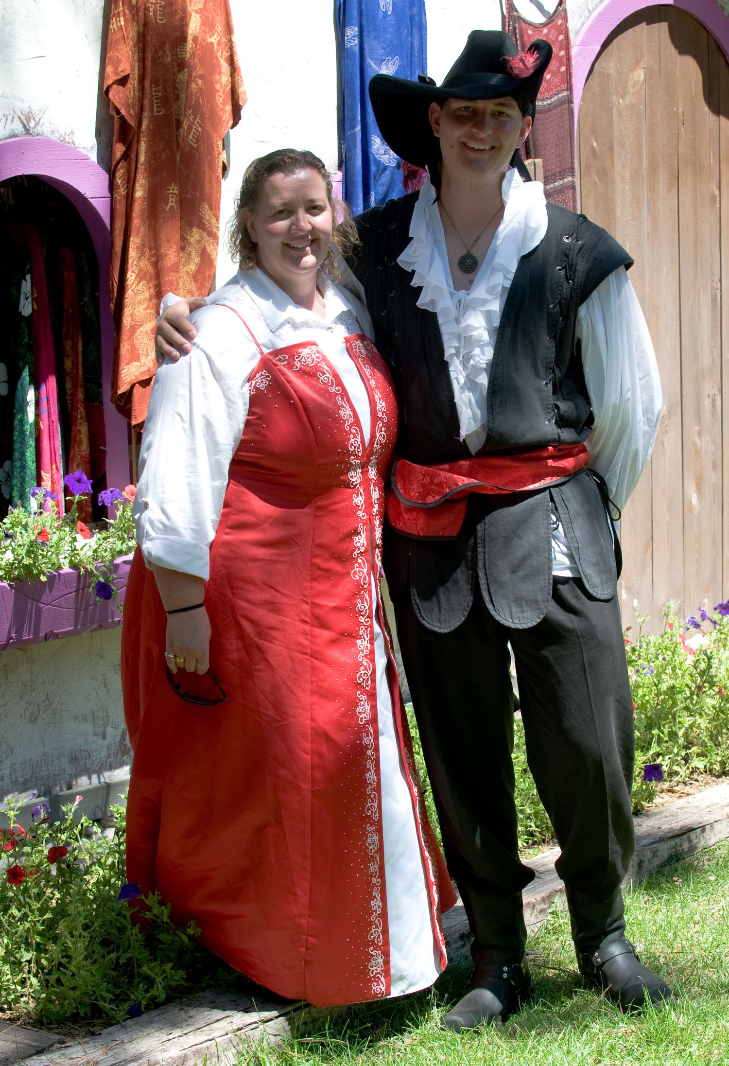 People in traditional Renaissance festival costumes with red dresses and white shirts pose outdoors.