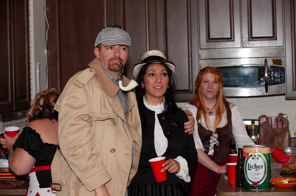 Three people in casual and formal attire gather in a kitchen with a bottle of Heineken visible on the counter.