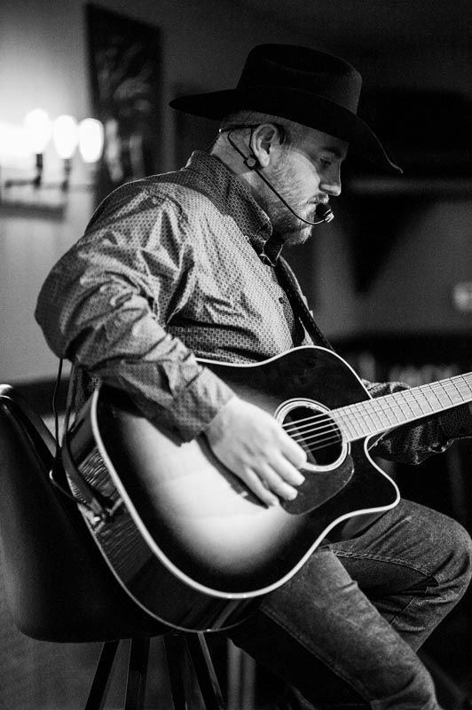 Black and white photos of musician playing acoustic guitar in casual attire.