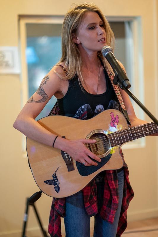 Musician performing with acoustic guitar and microphone in bright indoor setting.