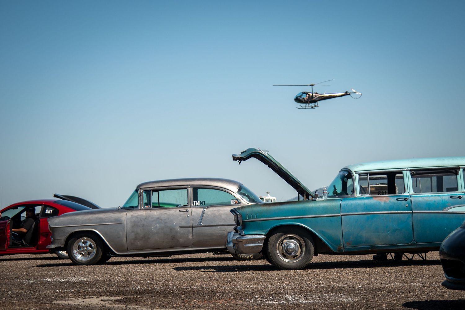 Classic American cars in the foreground with a helicopter flying above.
