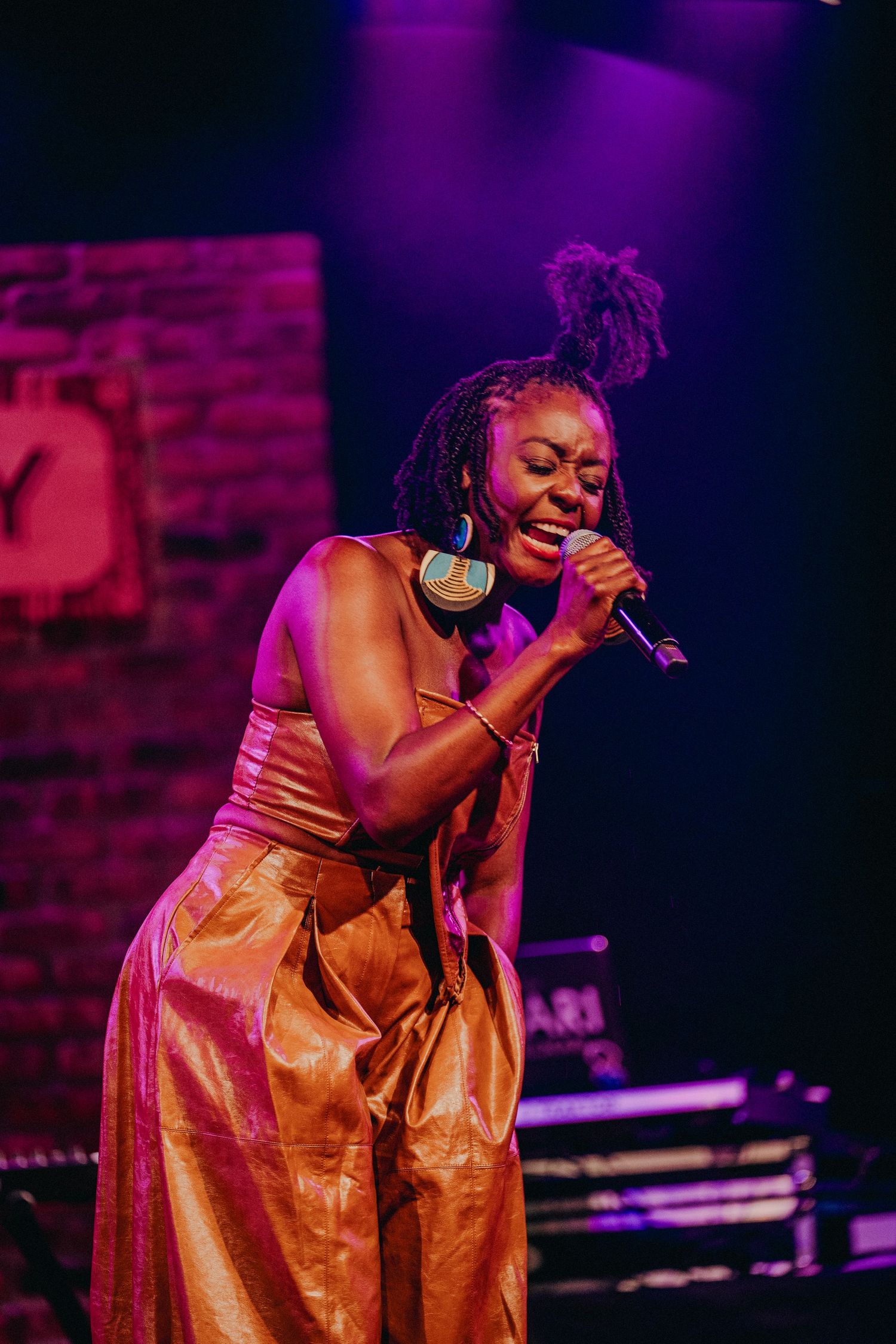 Young woman singer performing on stage in golden outfit holding microphone under purple lights.