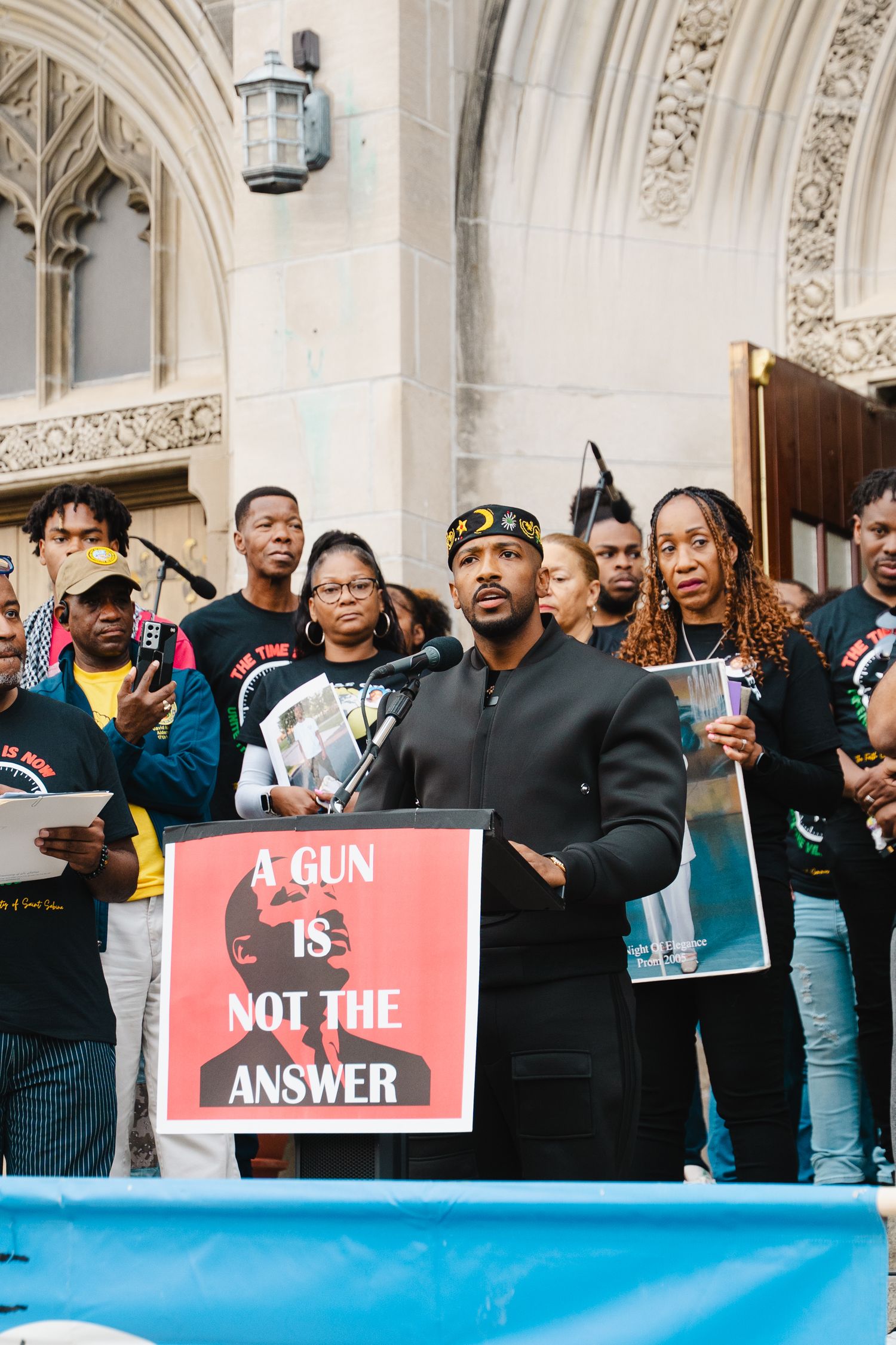 Man speaking at outdoor anti-gun violence rally at a podium with sign reading A Gun Is Not The Answer.