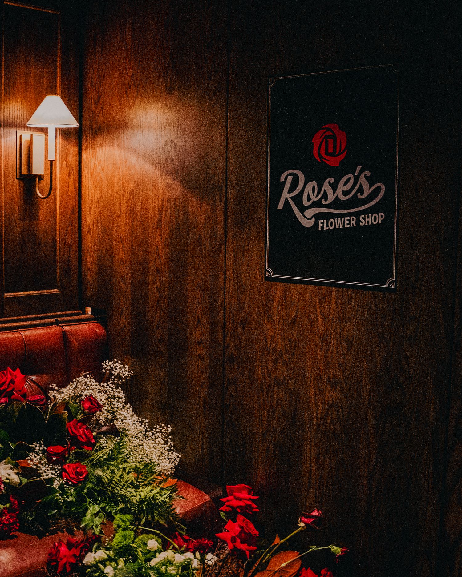 Rose's Flower Shop sign on wood-paneled wall with red flowers and warm lamp light.