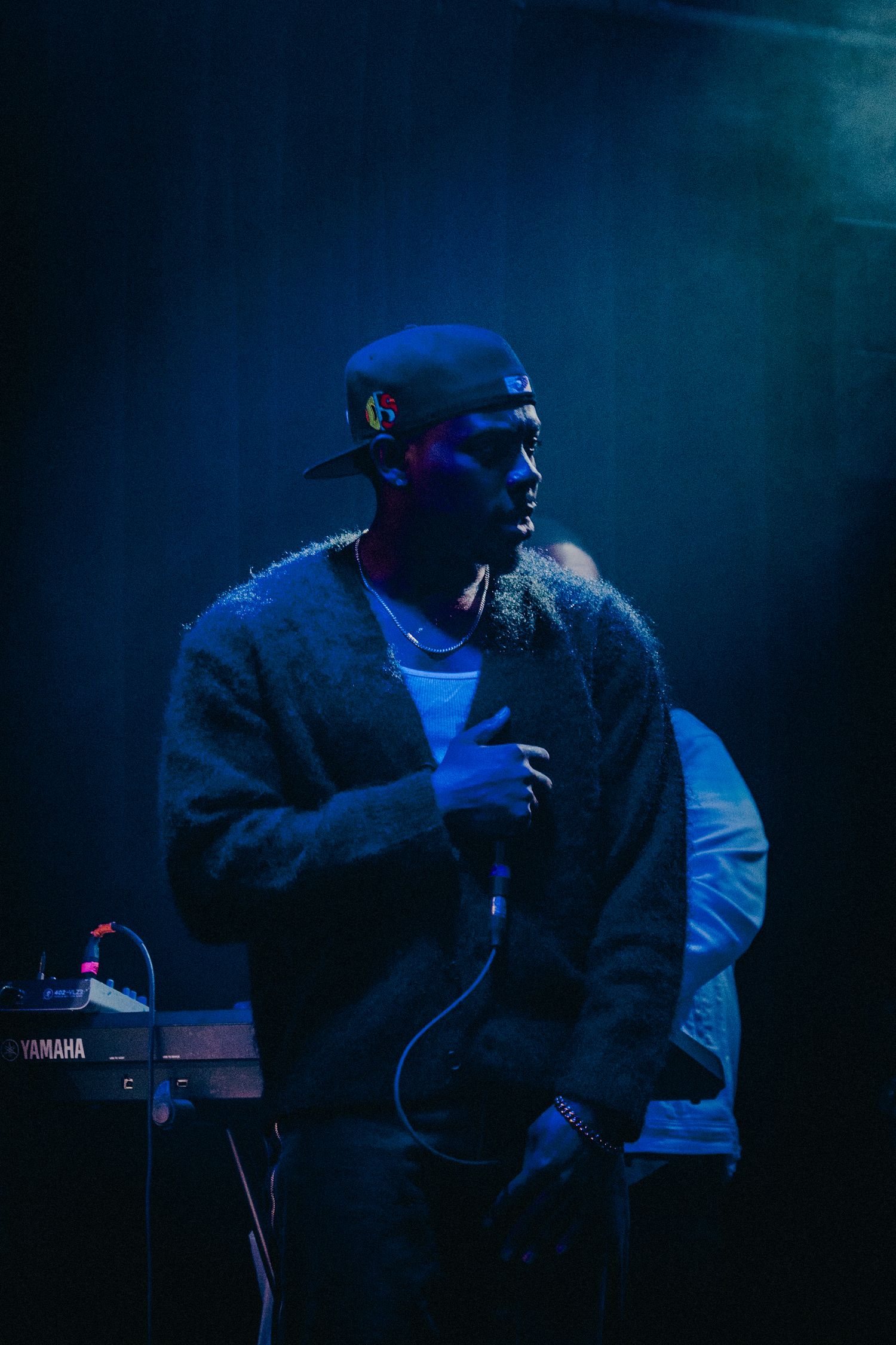 Male performer holding microphone on stage bathed in dramatic blue lighting at a live concert.