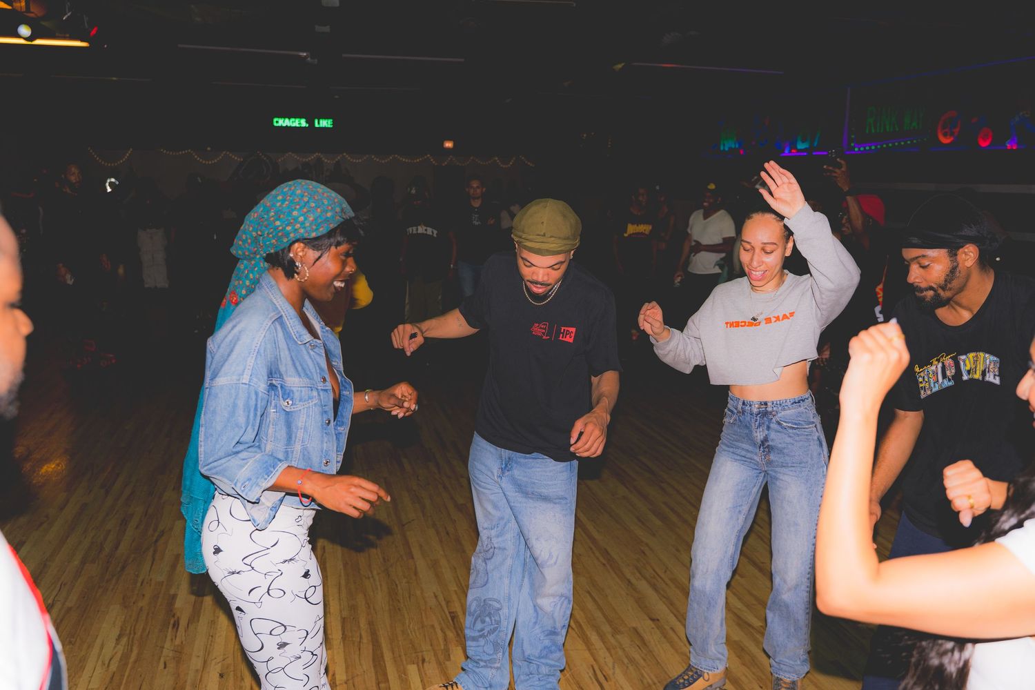 Group of friends dance together on a roller rink dance floor under colorful lights.