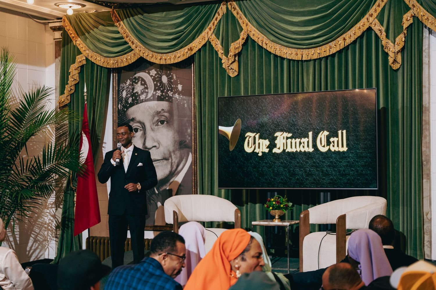 Speaker addresses seated audience at The Final Call event with portrait backdrop.