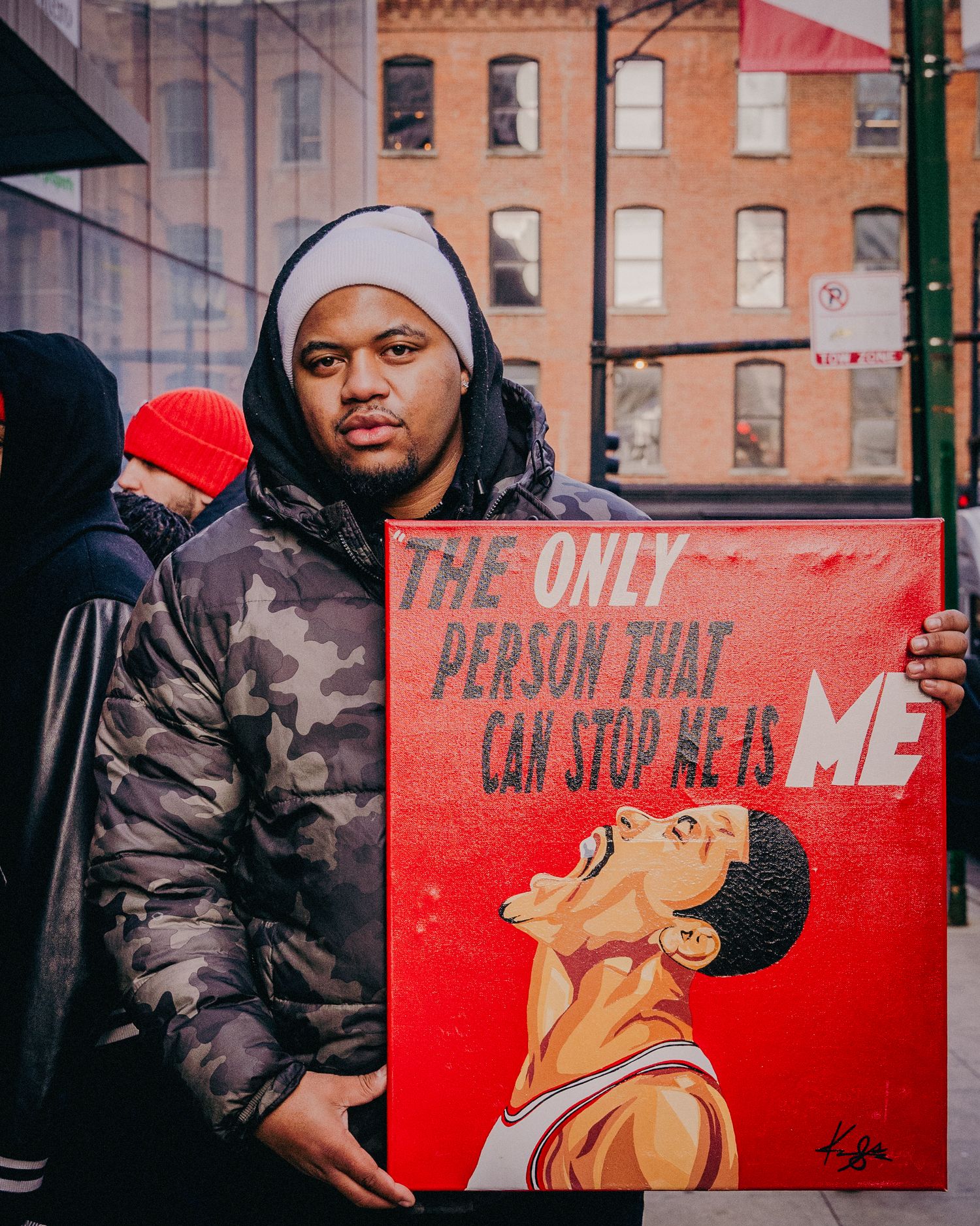 Man holding red painting reading 'The Only Person That Can Stop Me Is Me' on city street.