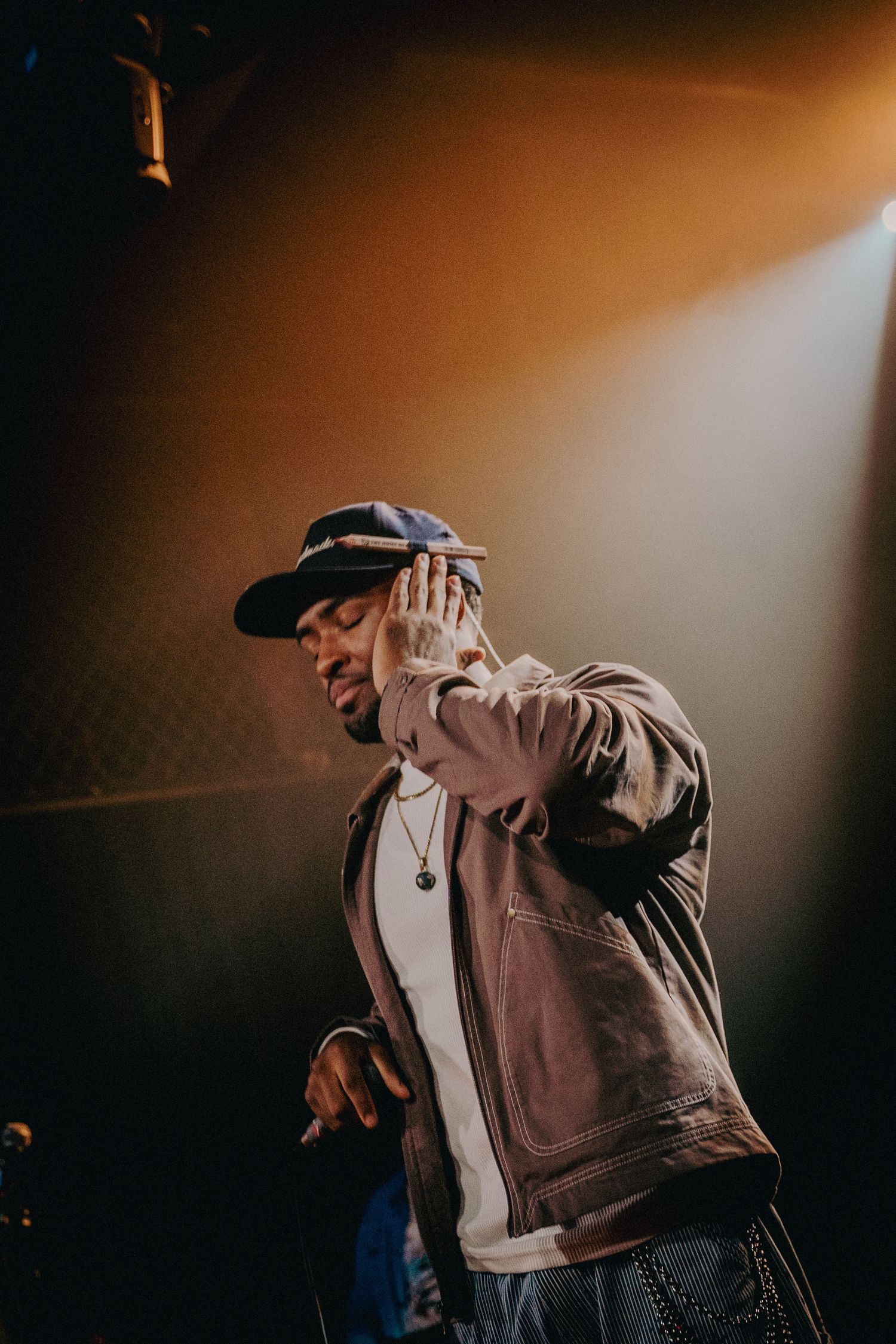 Male hip-hop artist gesturing on stage under dramatic warm spotlight at a live performance.