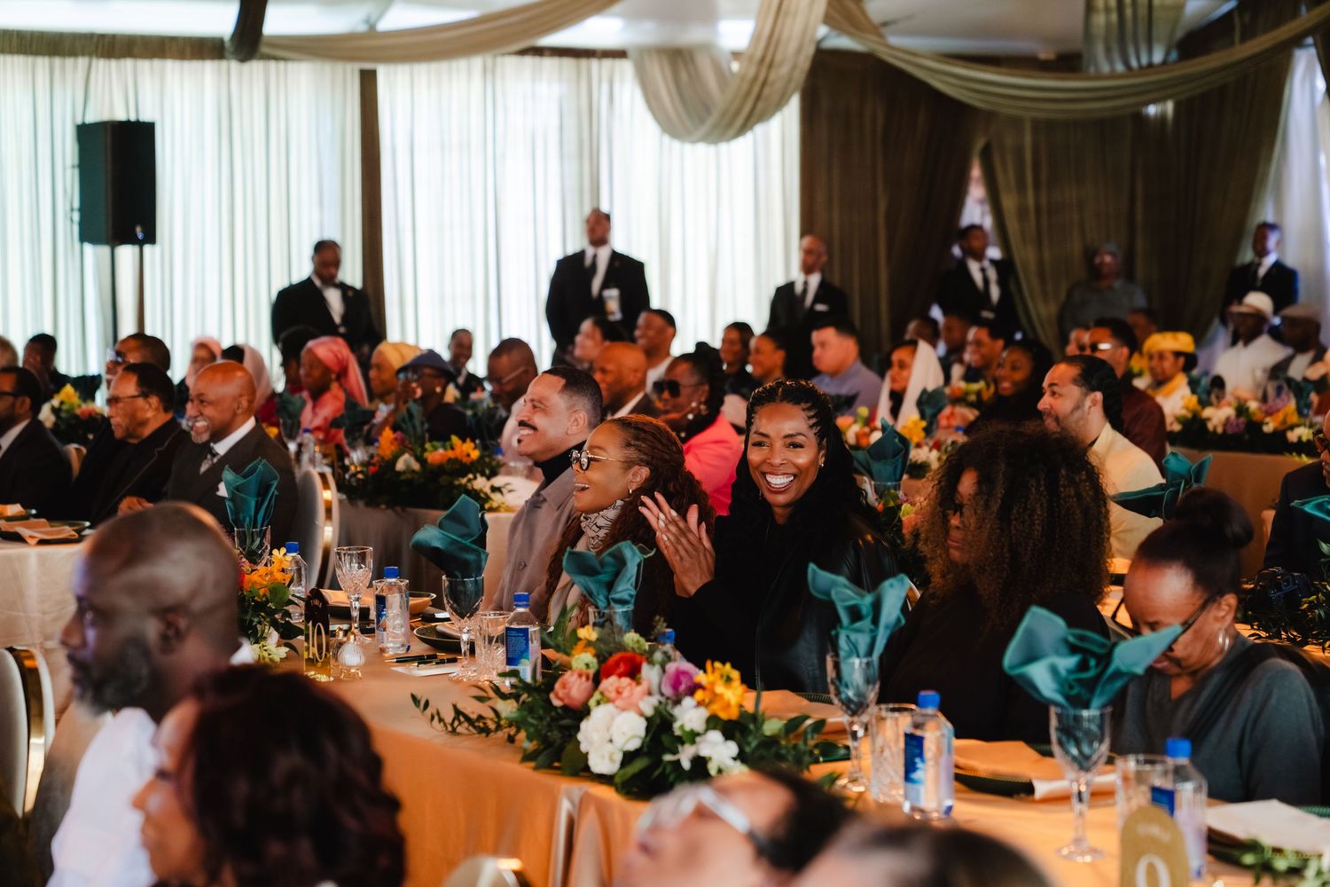 Guests celebrating at a formal banquet hall with colorful floral centerpieces and teal decor.
