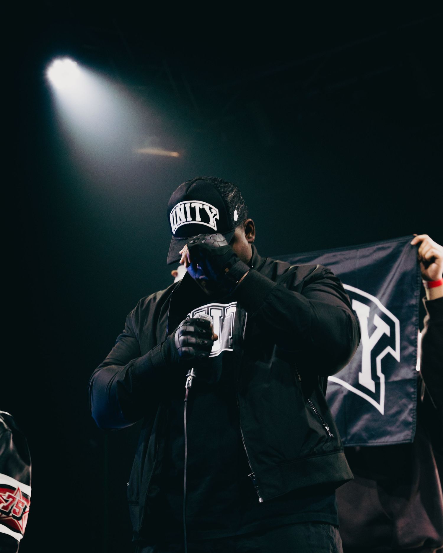 Performer on stage holding Unity flag under dramatic spotlight in dark venue.