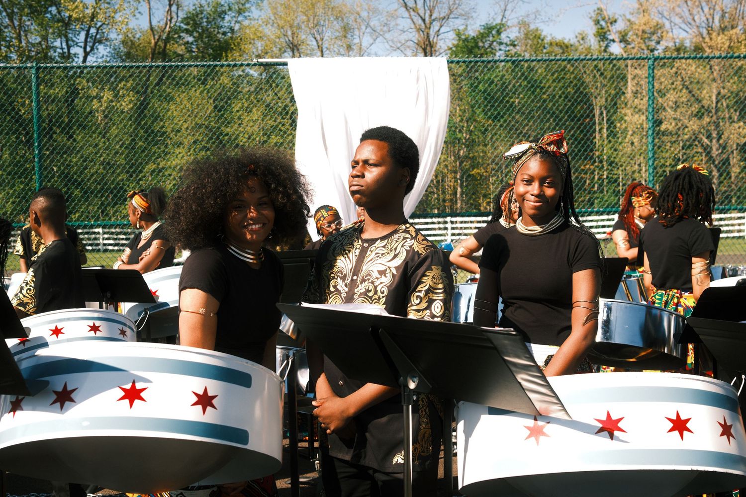 Three young women playing steel drums with Chicago flag design at an outdoor event.