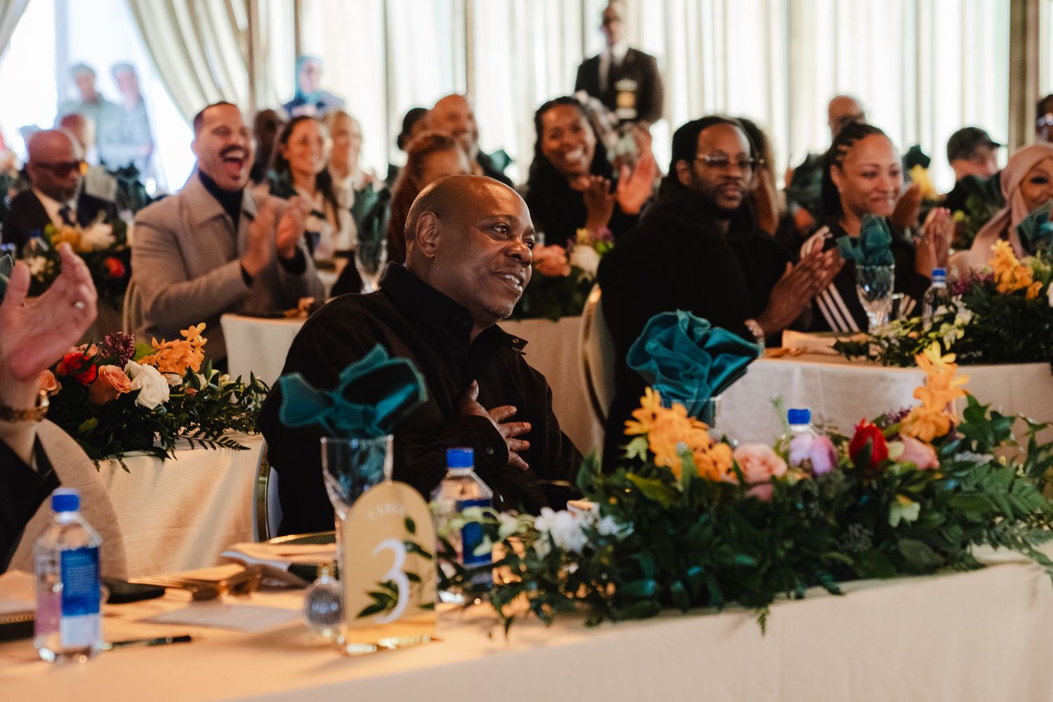 Man laughing joyfully at head table during formal banquet with floral centerpieces.