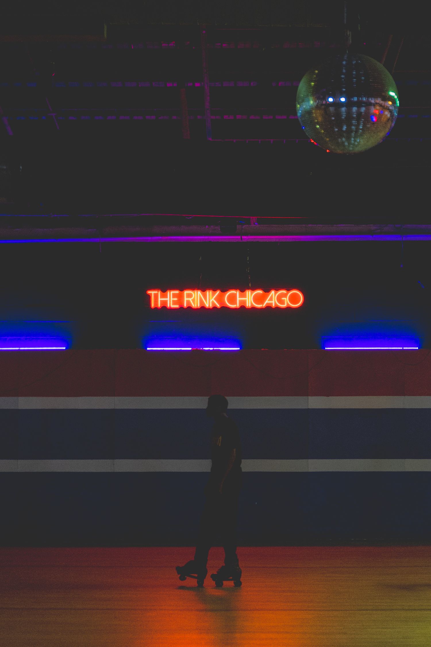 Person on roller skates at The Rink Chicago under disco ball and neon sign.