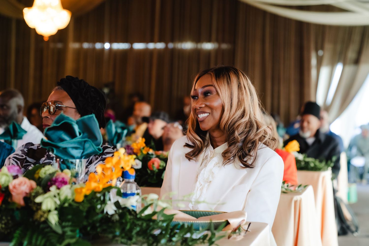 Smiling woman with blonde hair at elegant floral event table in white outfit.