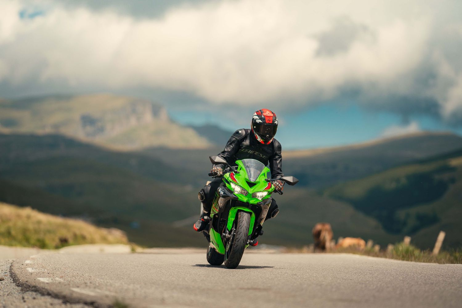 Motorcycle riders leaning into curves on a scenic mountain road with cloudy skies.