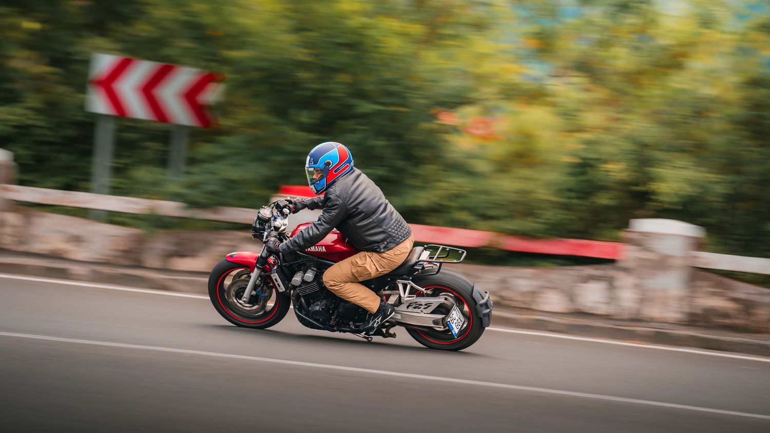 Motorcycle riders navigate a winding mountain road through lush green forest scenery.