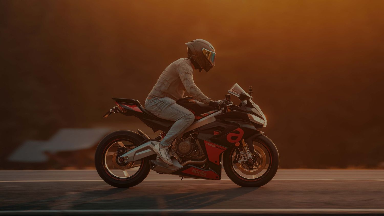 Sport motorcycle silhouetted against warm orange sunset on an empty road.