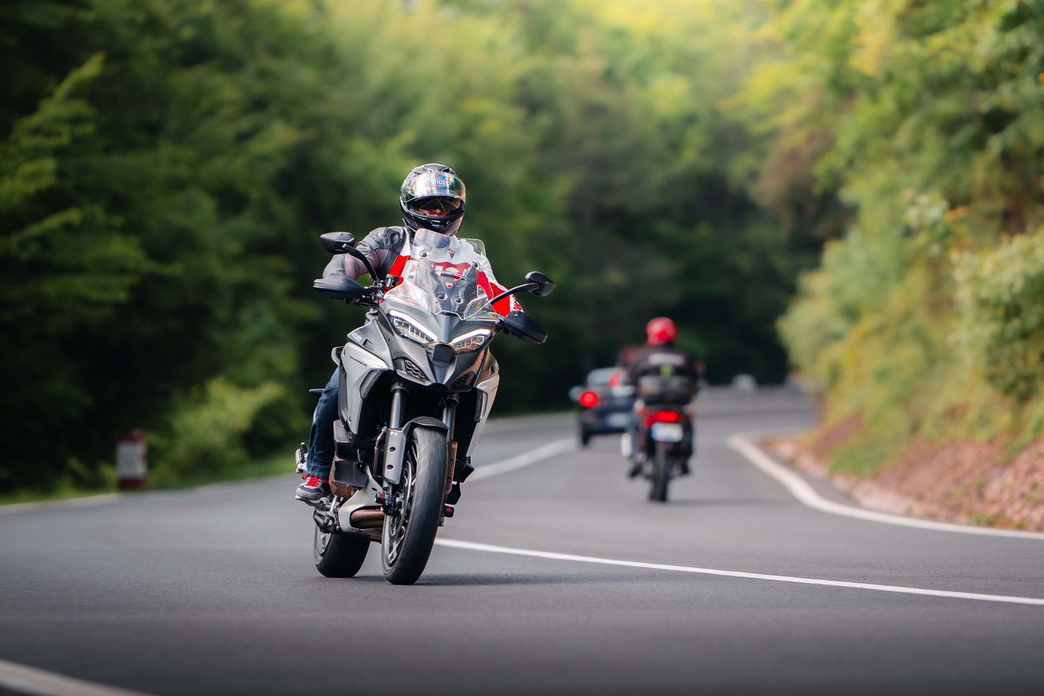 Sport bikes carving through curved mountain roads surrounded by green forest.