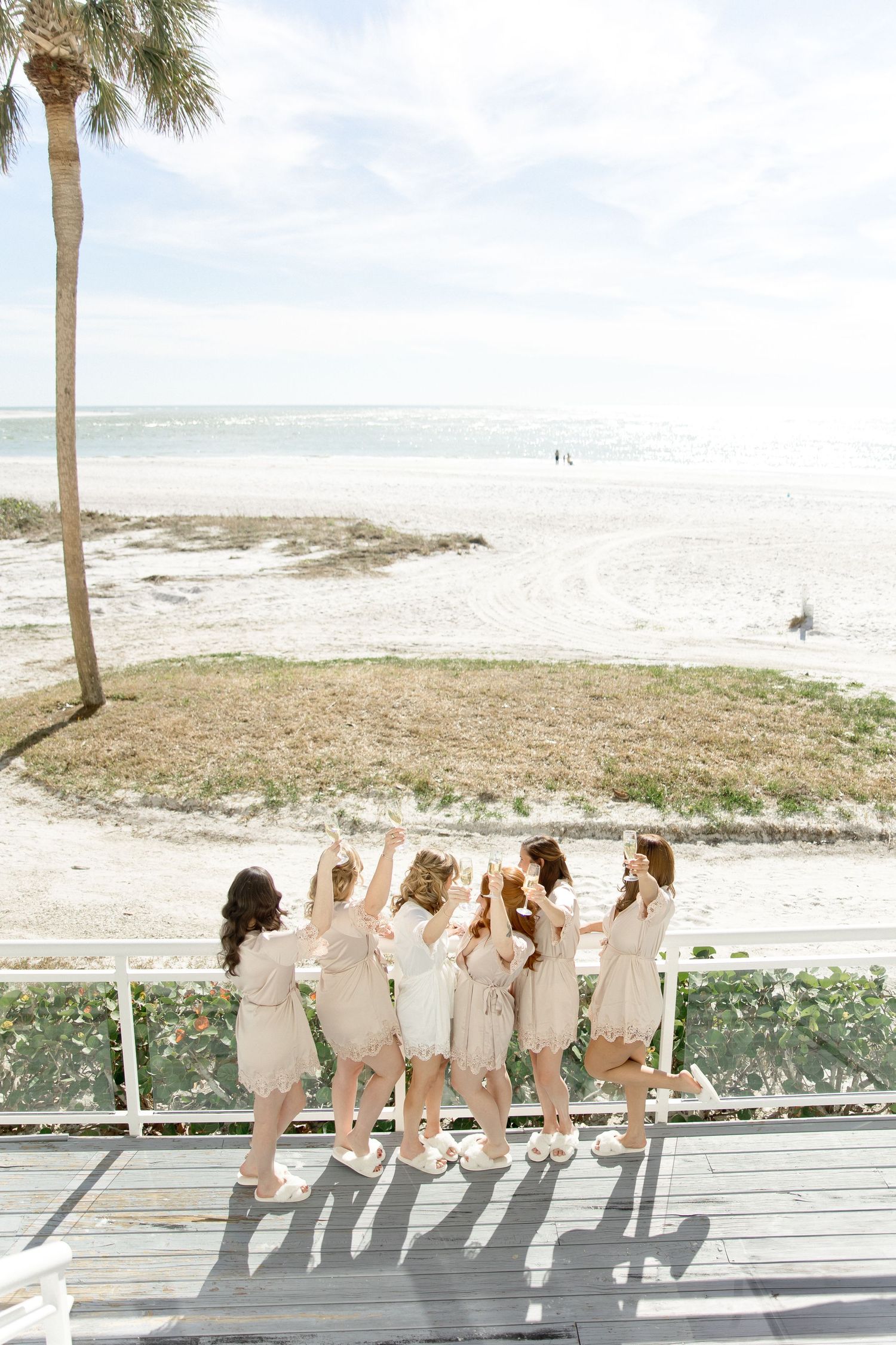 Bridesmaids in matching sage green dresses pose playfully on a beach boardwalk with ocean views.