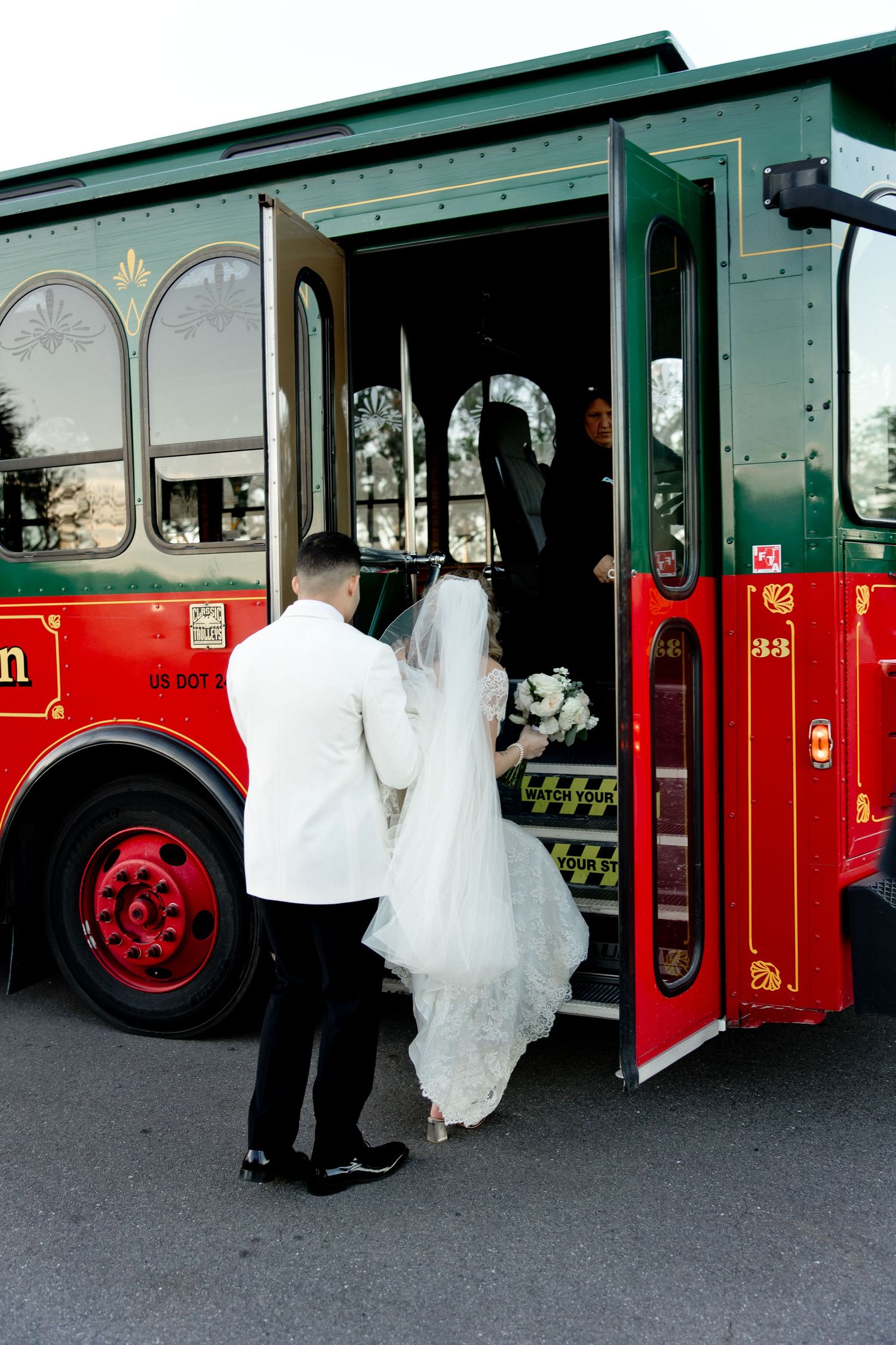 Wedding couple boarding a vintage red trolley car in formal attire.