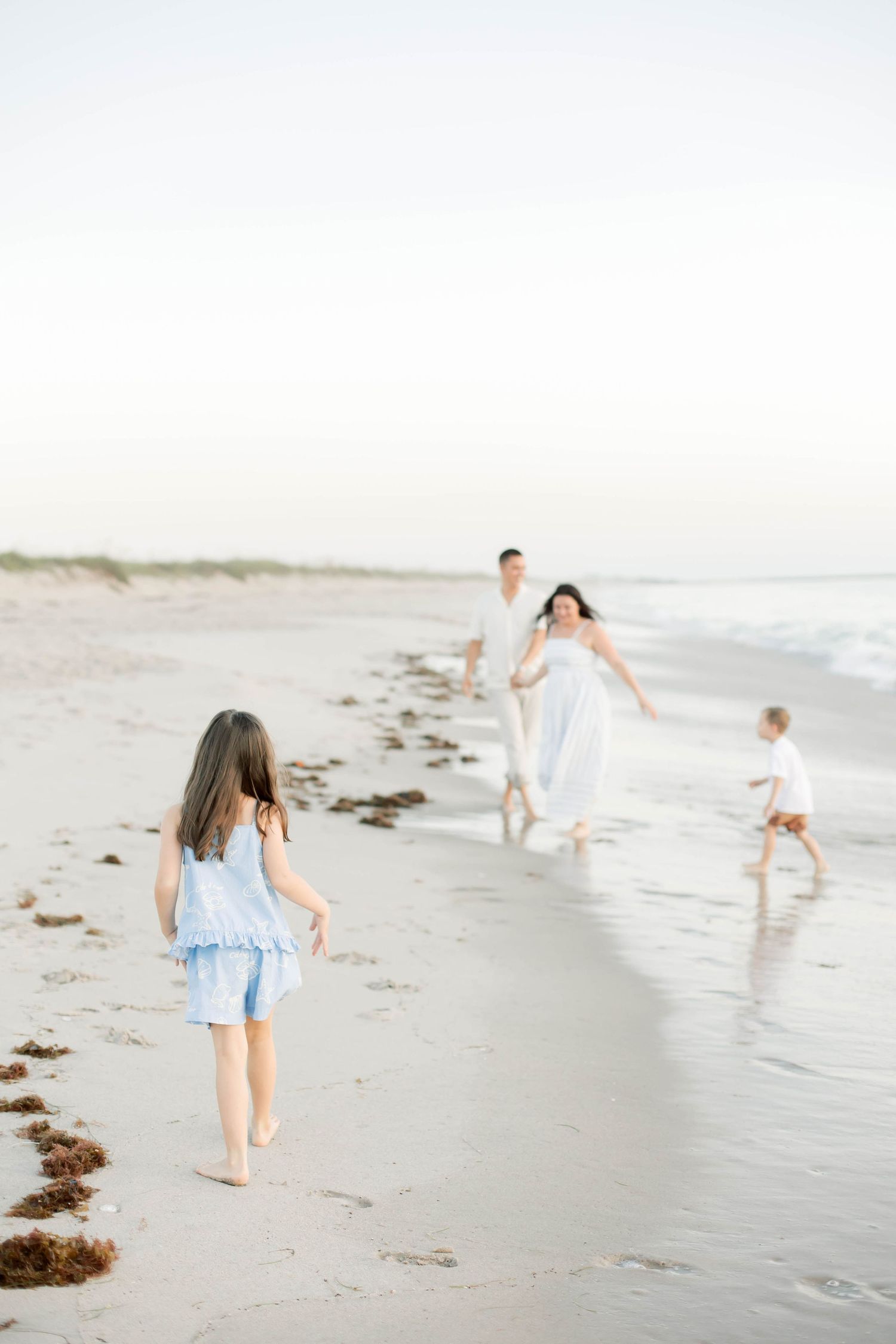 Family playing and running along beach shoreline at sunset.