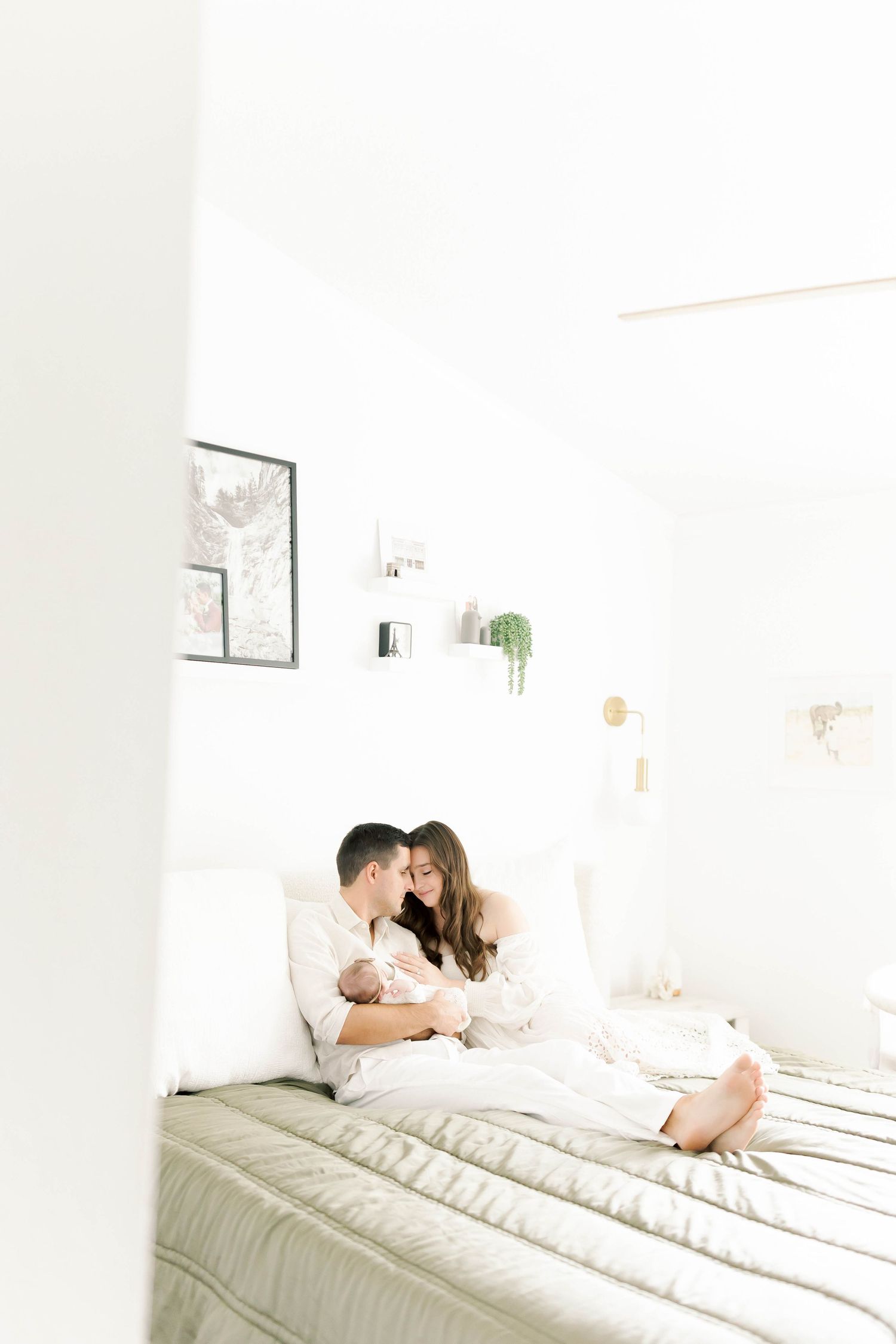 Couple lying together on white bedding in bright minimalist bedroom setting.