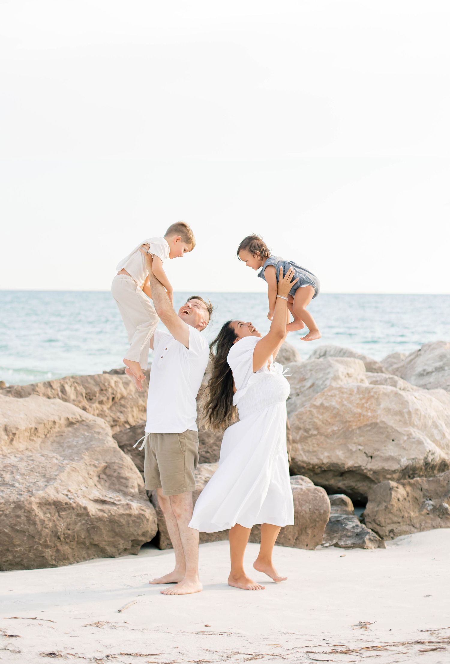 Family playing together on a sunny beach with large rocks in the background.