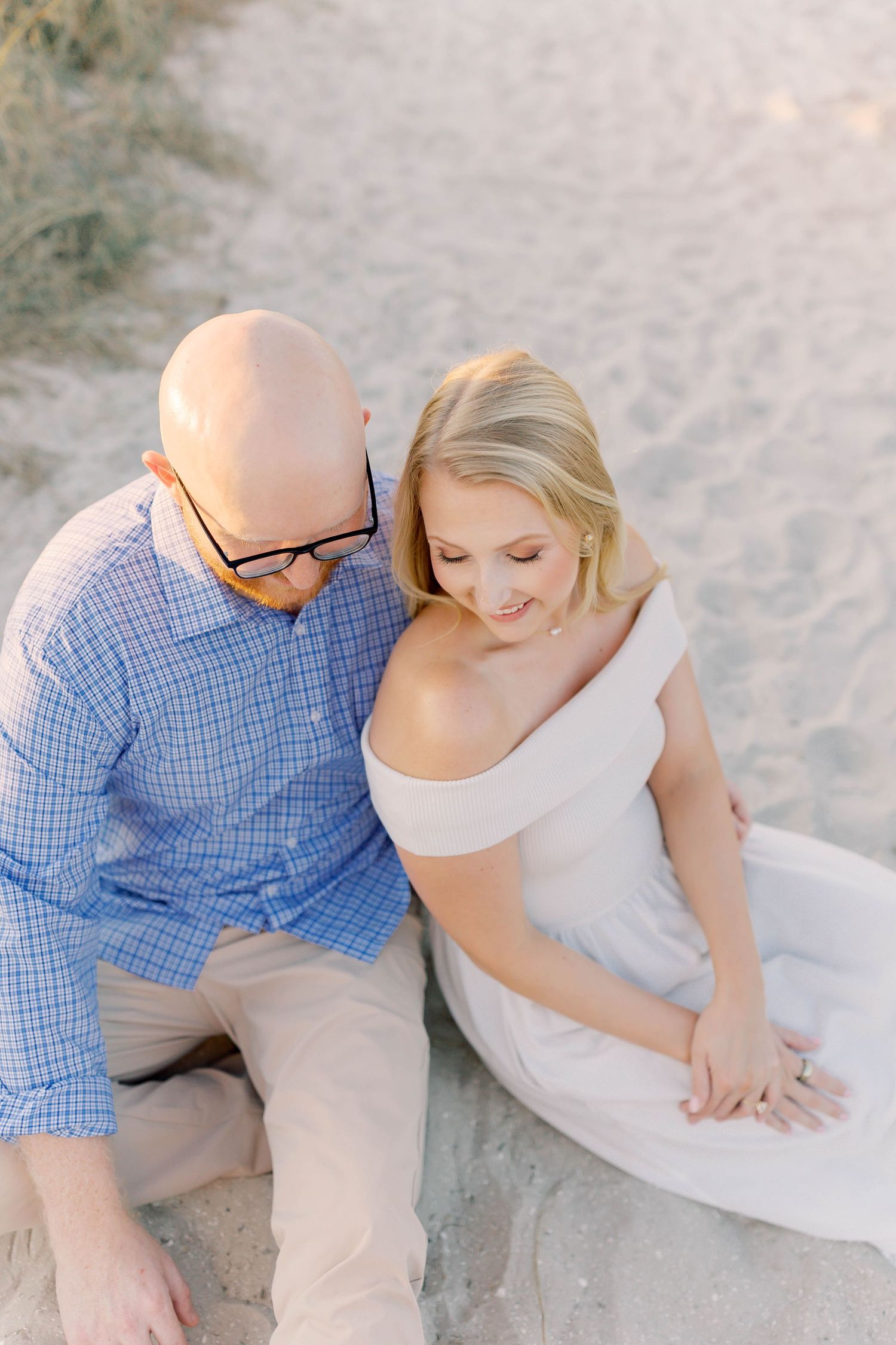 Intimate beach portrait with couple in blue and white against sandy background.