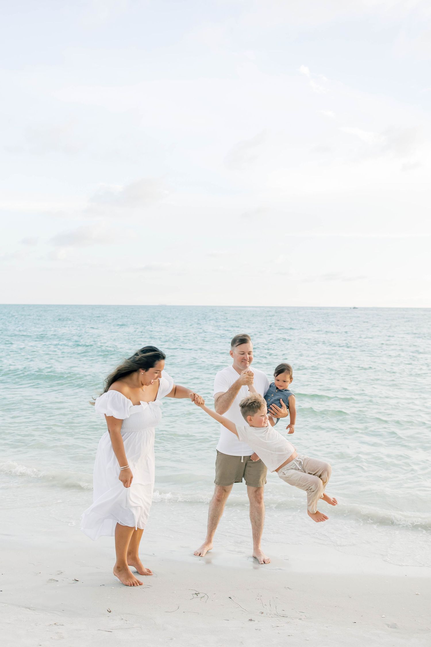 A family plays together on a pristine white sand beach with turquoise waters in the background.