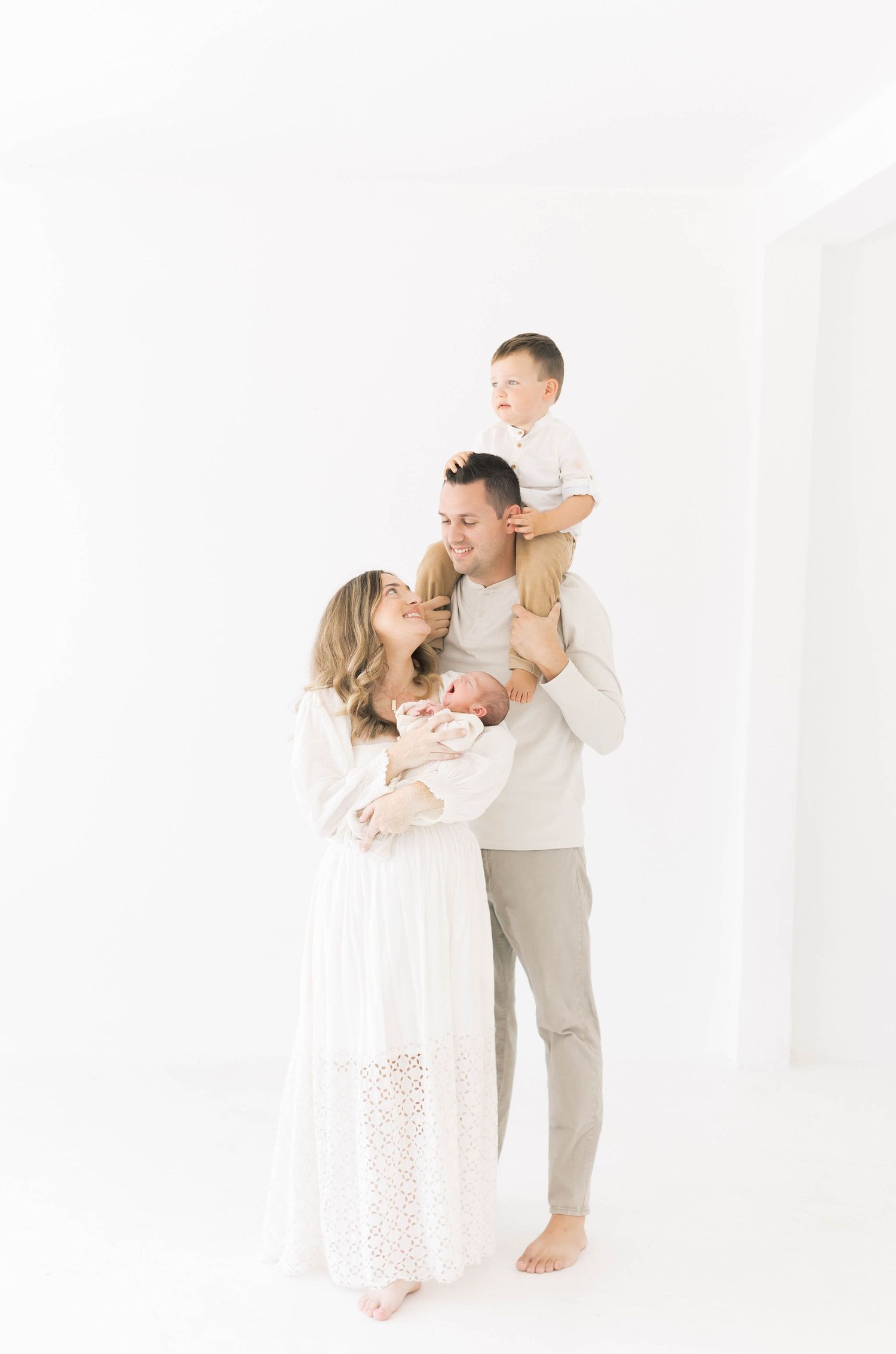 A loving family portrait in coordinated white and beige outfits against a bright background.