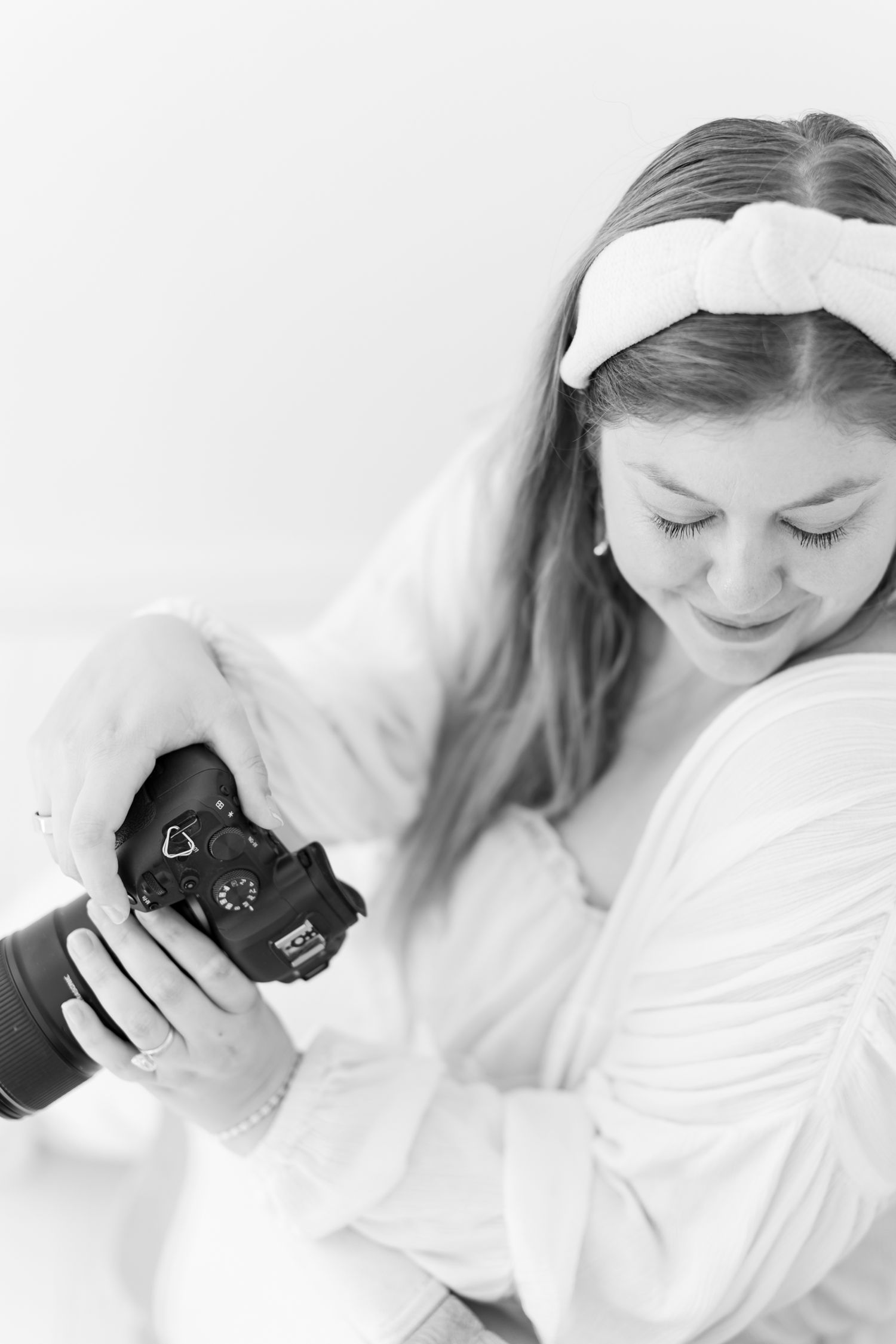 Black and white portrait of photographer examining camera in soft lighting.