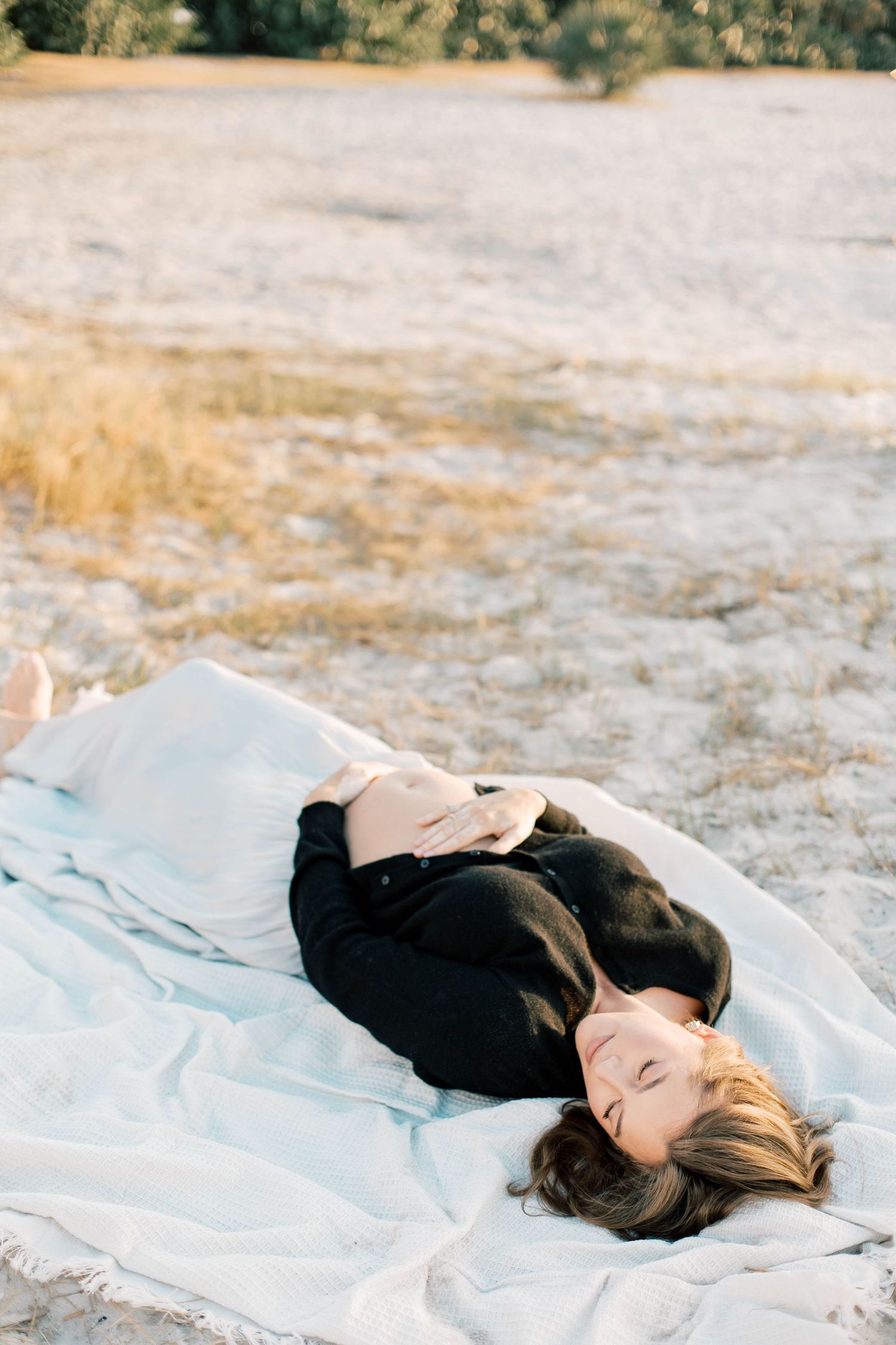 Person relaxing on light blue blanket in natural outdoor setting.