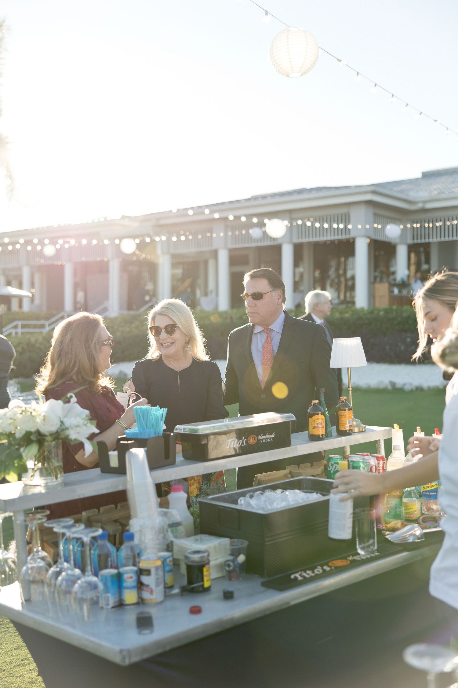 Wedding guests enjoying drinks at an outdoor bar during sunset.