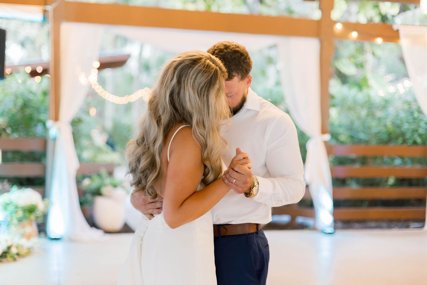 Couple sharing their first dance in an outdoor reception area with natural lighting.