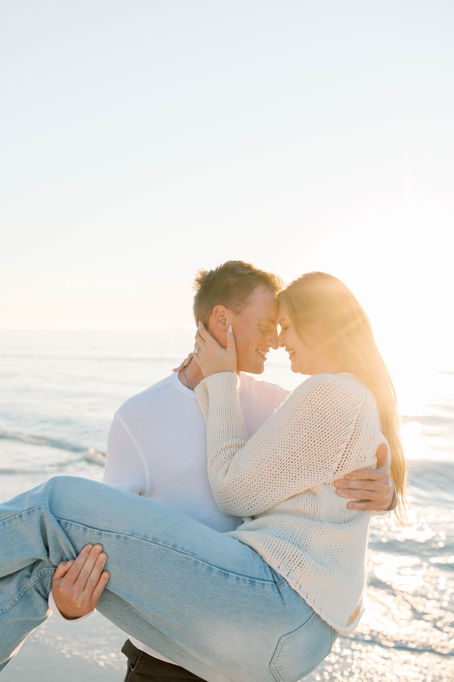 A romantic beach scene with a couple embracing in casual white outfits at sunset.