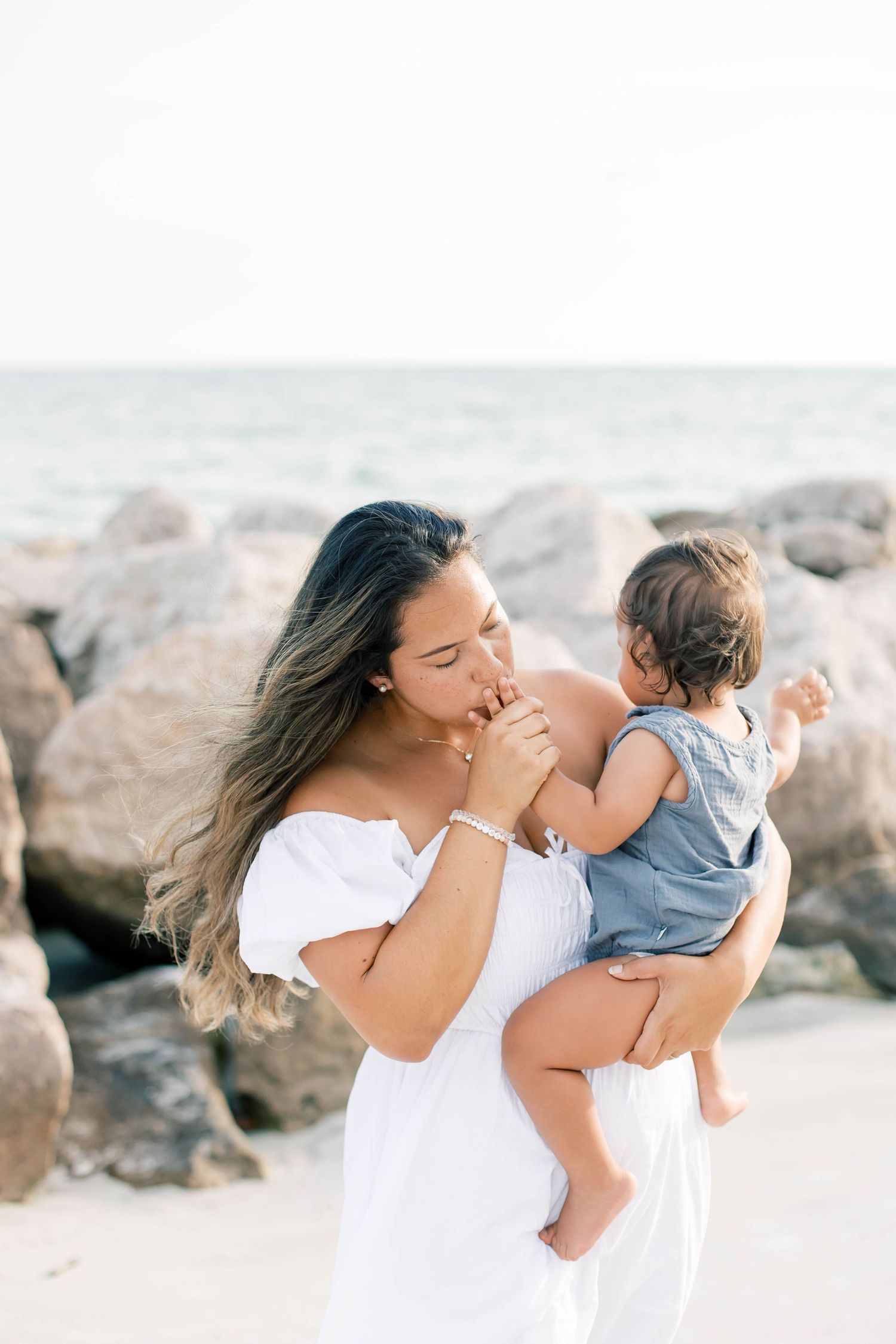 Candid family moments captured on a bright beach with rocky coastal backdrop.