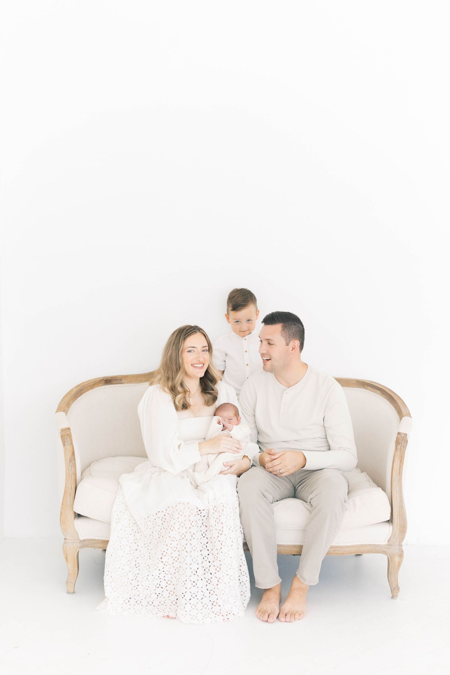 Family lounging on beige settee sharing intimate moments in bright studio setting.