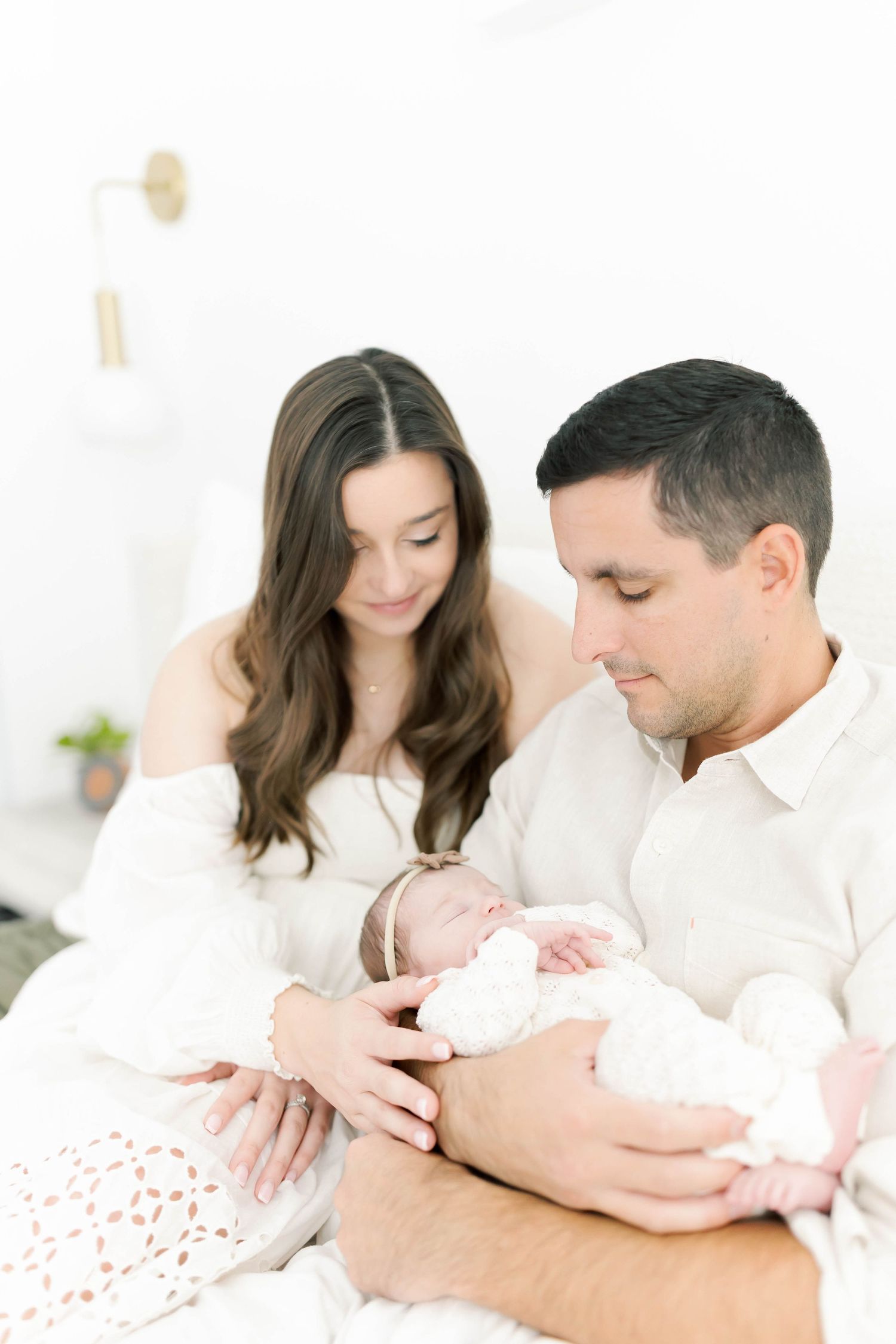 Parents in white clothing bonding with their newborn baby in bright setting.