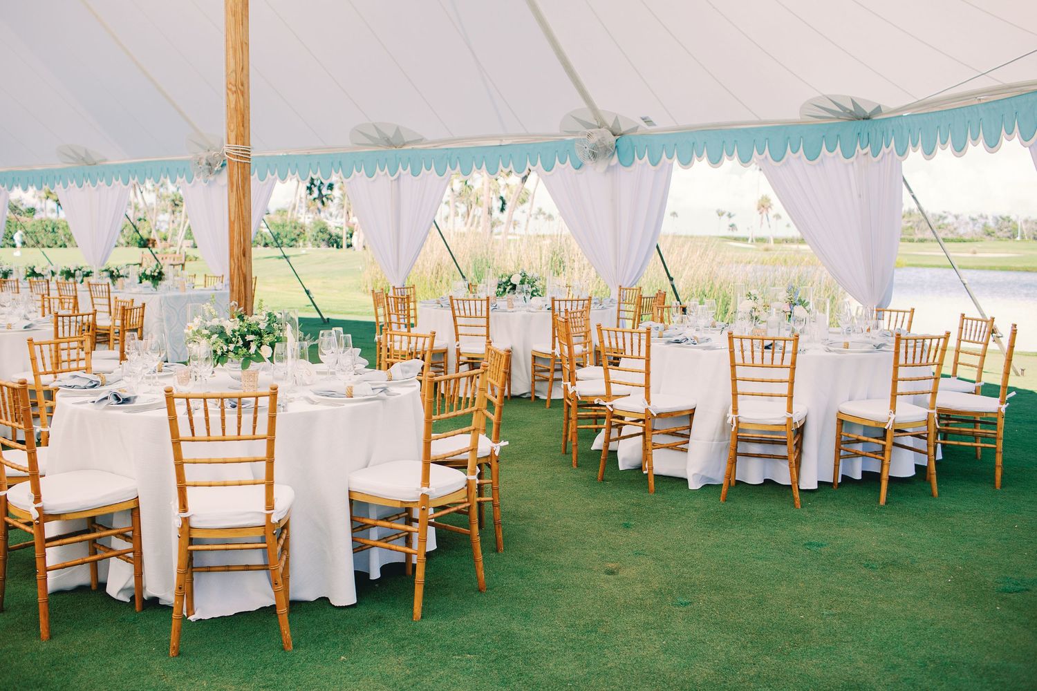 Wedding reception tent interior with long tables and wooden chairs arranged in rows.