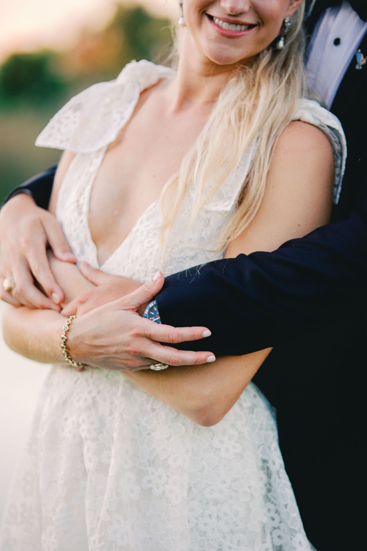 Close-up wedding photos showing details of white lace dress and hands with jewelry in natural outdoor lighting.