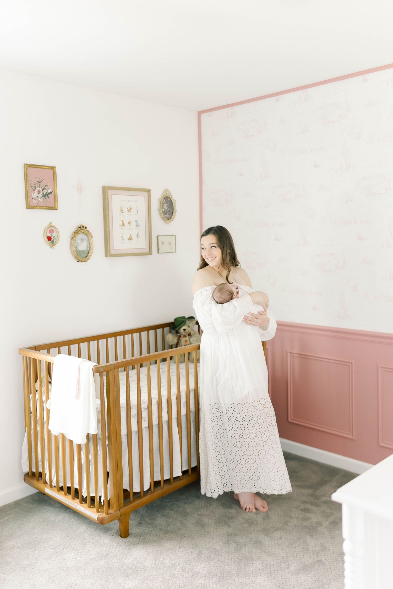 A nursery room with wooden crib, framed wall art, and someone holding an infant.
