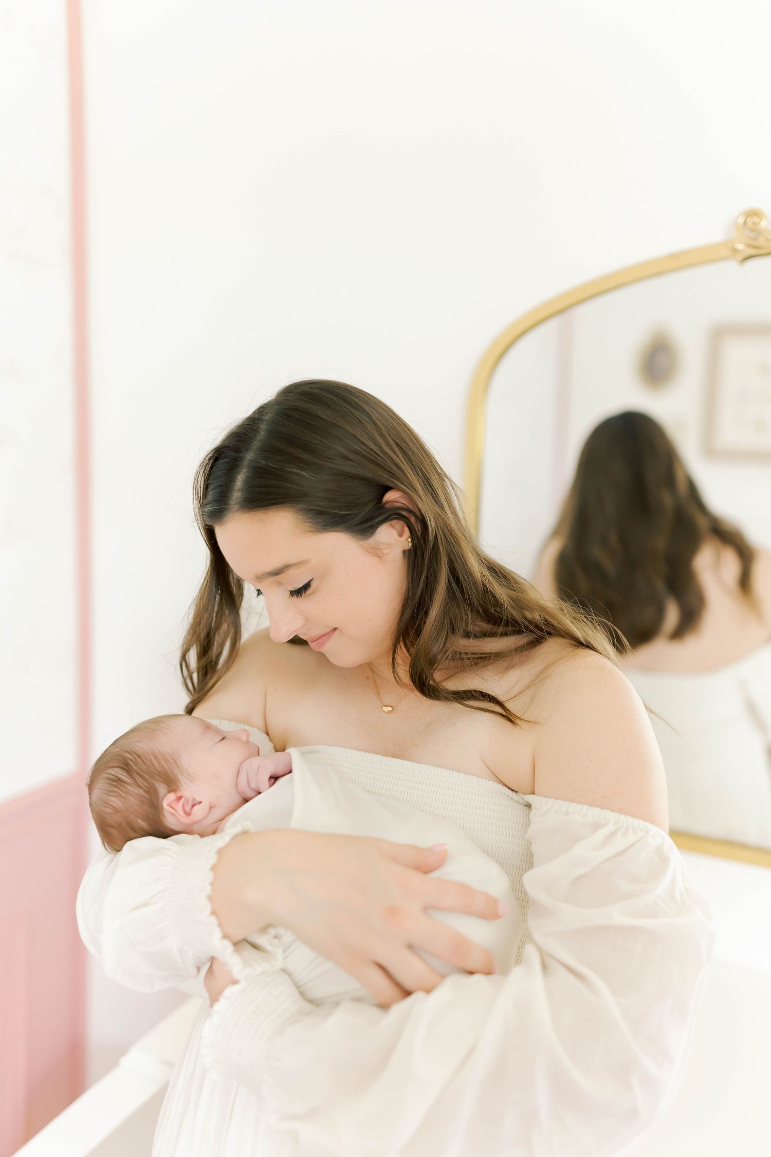 An intimate moment between parent and newborn in a softly lit nursery with pink walls.